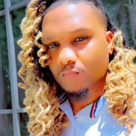 A person with long, curly blonde hair is posing outdoors with a serious expression.