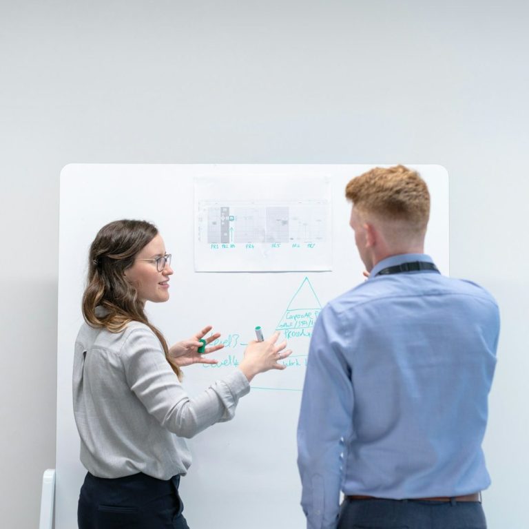 A woman gestures while discussing a chart with a man in a professional setting.