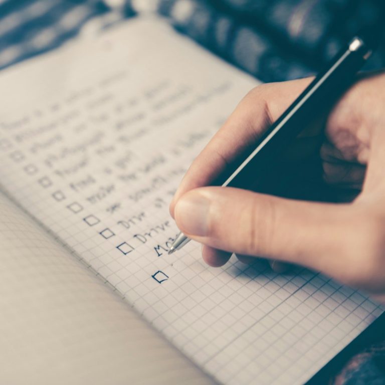 Handwritten Checklist Hand holding a pen, checking items on a notepad filled with lists and checkboxes.