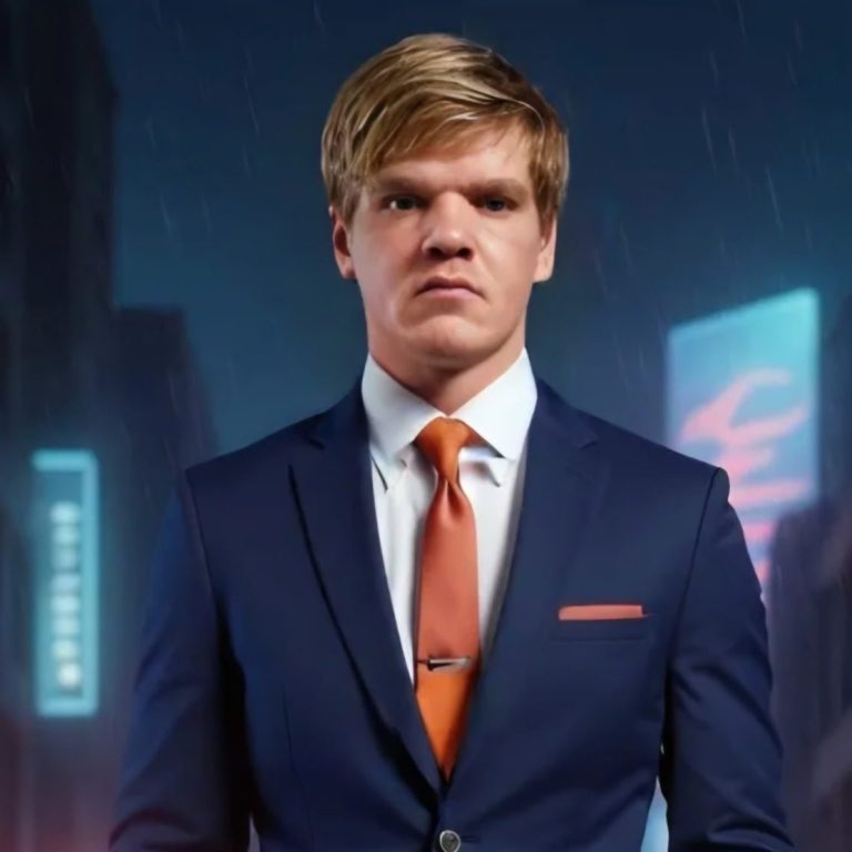 A young man in a dark suit with an orange tie, standing in a city at night.