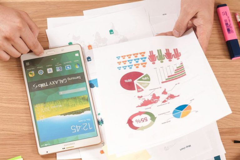 Graphs, Charts, and Dataset Hands holding a tablet and printed charts on a wooden desk.