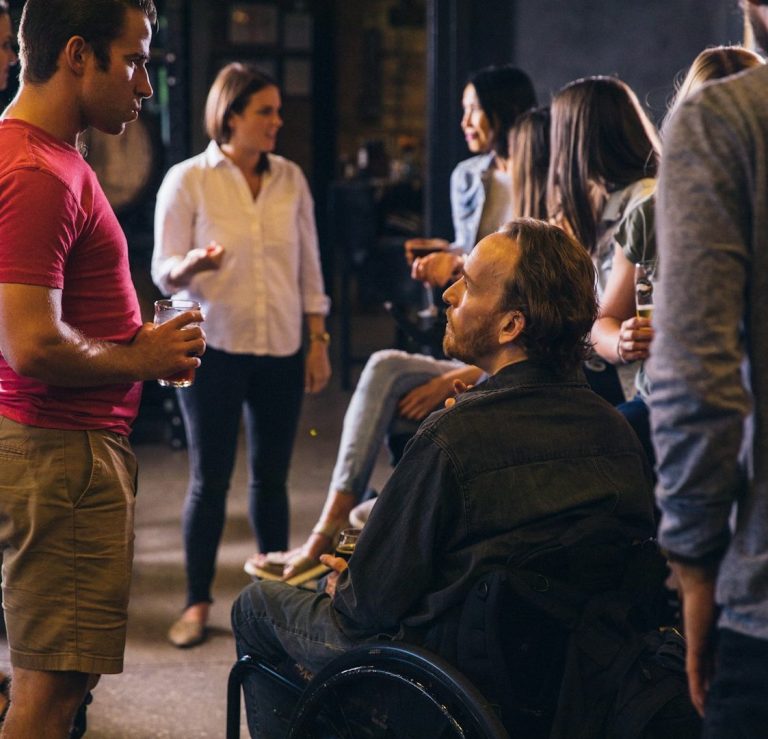 People engaging in conversation at a social gathering, including a person in a wheelchair.