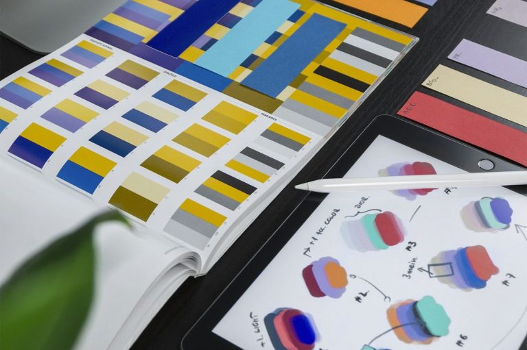 Color Design Chart Color swatches and design sketches displayed on a desk with a plant in the corner.
