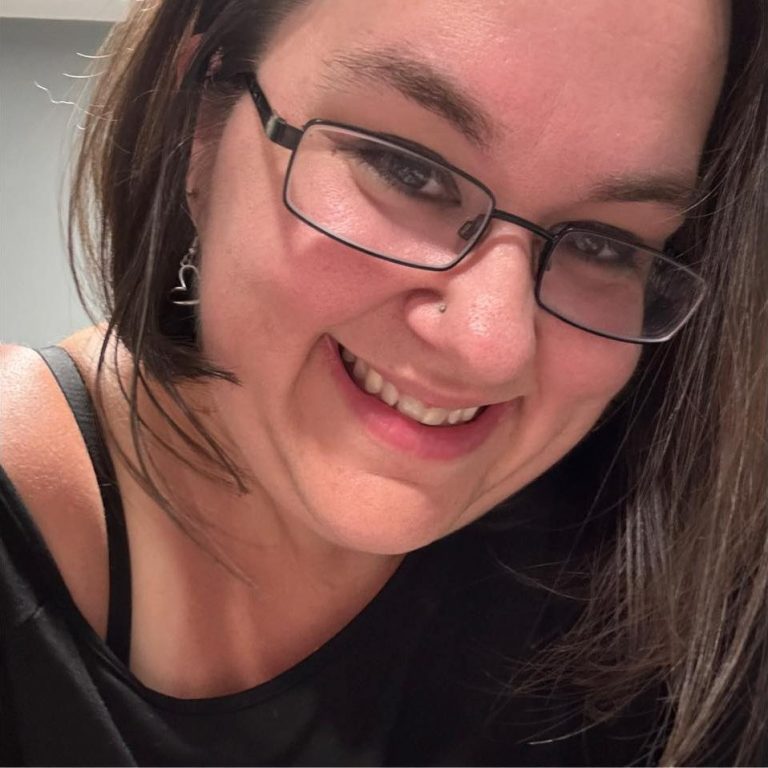 Smiling woman with glasses and dark hair, wearing a black top.