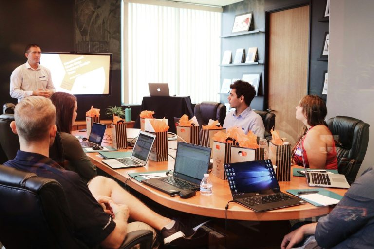 Group at Conference Table with Computers A group of people in a conference room listening to a presentation.